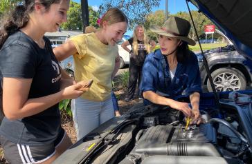 Image of two young women looking under bonnet of car with instructor 