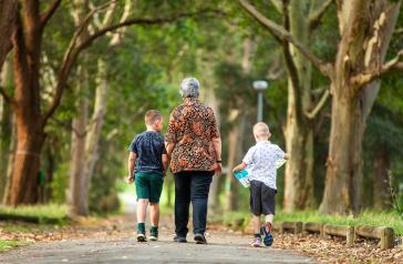 A grandmother and two children walking along a path between trees at Queen Elizabeth Park