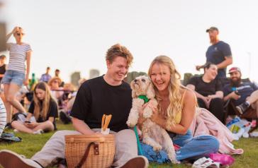 A young man and woman sitting on a picnic blanket and laughing