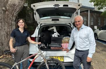 Mayor Michael Megna with member of Sustainability and Waste team standing in front of car packed with e-waste for recycling. Staff member stands with a bicycle. 